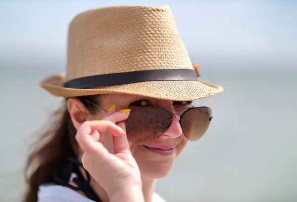Portrait de jolie fille en lunettes de soleil et chapeau, tenant des lunettes avec la main, regarde dans la caméra, gros plan — Photo