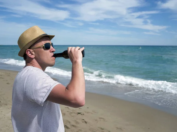 Jeune homme au chapeau boit de la bière debout au bord de la mer, copyspace — Photo