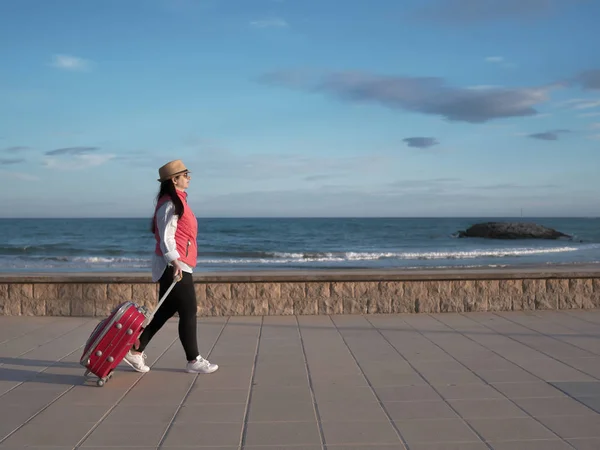 Fille touristique se promène le long de la promenade près de la mer avec une valise rouge — Photo