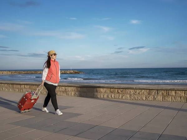 Fille marche le long de la promenade près de la mer avec une valise rouge — Photo