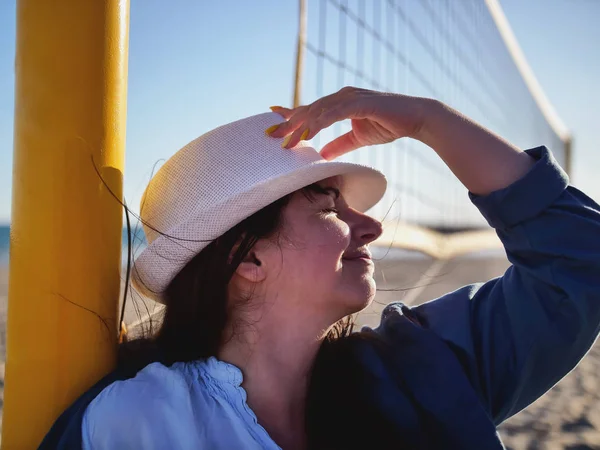 Portrait d'une jolie brunette coiffée d'un chapeau blanc se tient près d'un filet de volley-ball sur la plage — Photo