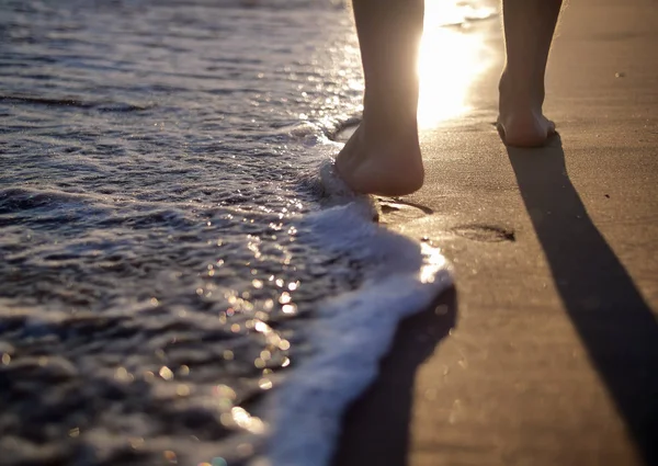 En mand går langs stranden, skummende bølger vasker sandet, solnedgang på stranden - Stock-foto
