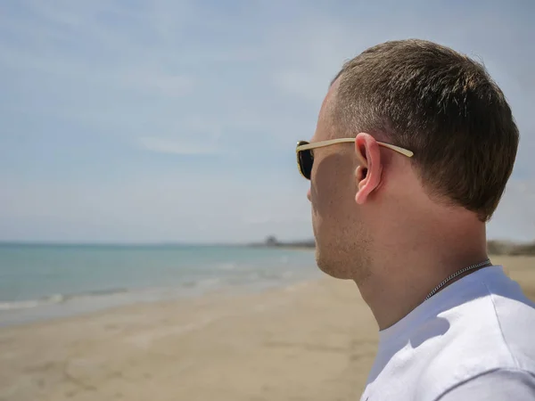 Un jeune homme en lunettes de soleil se tient seul près de la mer et regarde vers l'horizon — Photo