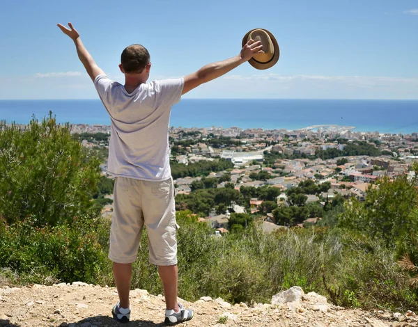 Touriste se tient au sommet d'une colline écartant les bras sur le côté, détient concept chapeau de voyage, liberté — Photo