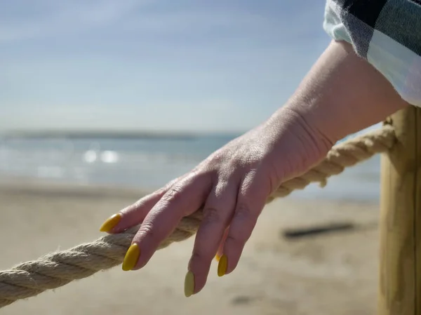 A female hand touches a rope stretched on a beach pier near the sea, the passage is closed, the end of the beach season — Stock Photo, Image