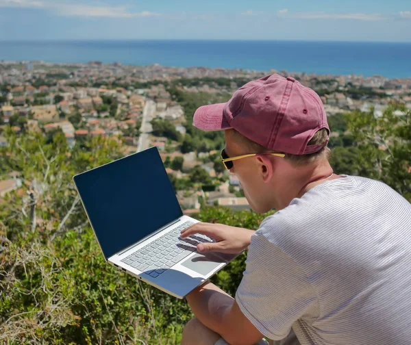 Портрет фрилансера, работающего на ноутбуке на горе рядом с приморским городом — стоковое фото