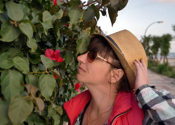 Attrayant jeune femme touristique voyageant autour de la ville en profitant de l'odeur d'une fleur rose en plein air — Photo