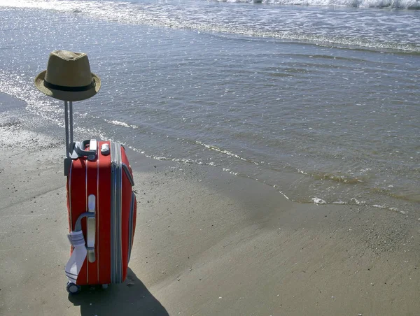 Une valise de voyage avec un chapeau sur une poignée se dresse sur la plage près de la mer. Concept week-end — Photo