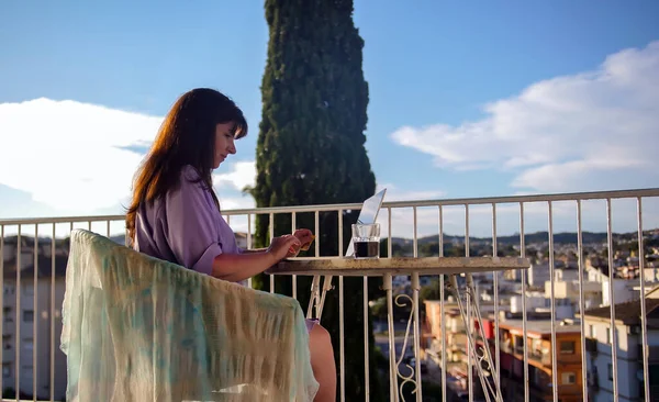 Belle femme brune assise sur un jour d'été ensoleillé sur le balcon avec un ordinateur portable — Photo
