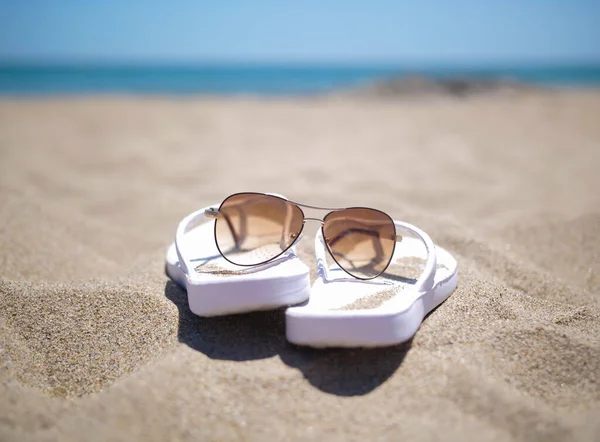Pantoufles blanches et lunettes de soleil sur une plage de sable, concept vacances — Photo