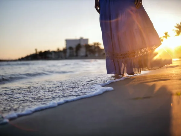 Une fille avec une jupe bleue se promène le long de la plage au coucher du soleil — Photo