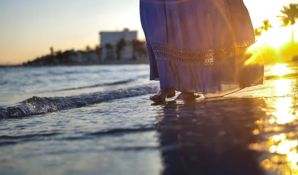 Uma menina em uma saia longa azul caminha sozinha ao longo da praia durante um belo pôr do sol Fotografias De Stock Royalty-Free