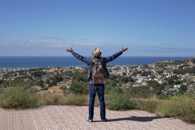 Sırt çantalı bir gezgin, bir dağın tepesinde dikilirken kollarını kaldırdı.