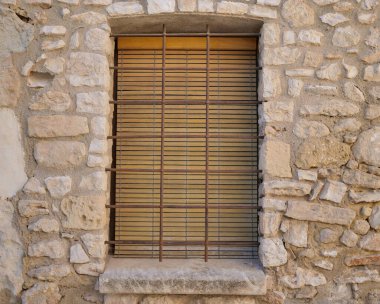 Closed window with wooden shutters and bars with a stone window sill in the old wall of the house