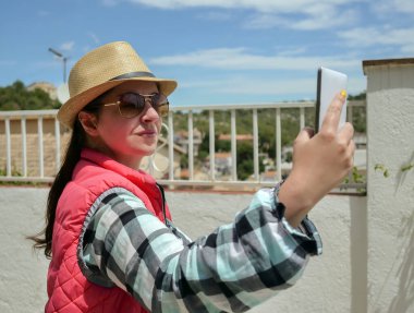 Şapkalı genç esmer, beyaz cep telefonundan selfie çekiyor.