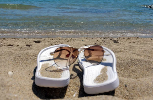 Pantoufles et lunettes blanches pour femme sur une plage de sable, concept vacances — Photo