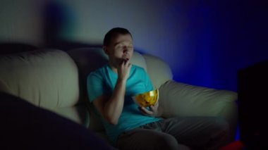 Komik bir film izleyen bir adam gece geç saatlere kadar TV karşısında elinde cipsle koltukta oturuyor.
