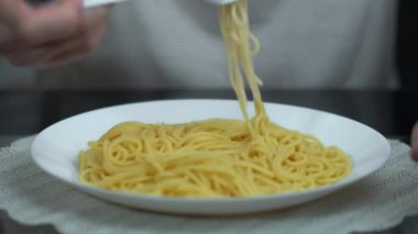 Beyaz bir tabakta spagetti, bir adam çatala sarılıp yiyor, yakın plan.