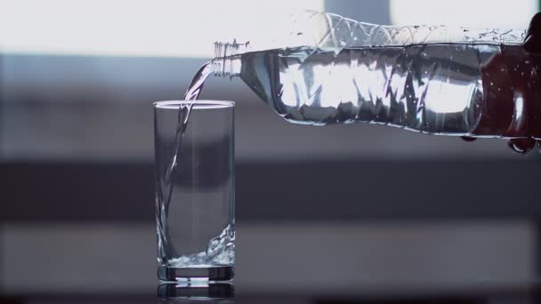 一个人把塑料瓶里的清澈的水倒入玻璃杯中 放在窗户的后面 — 图库视频影像