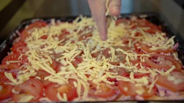 Adam evde pizza pişiriyor, üzerine peynir serpiştiriyor, ev yapımı yemekler yapıyor.