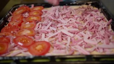 Ev yapımı pizza pişiren bir adam pizzaya taze doğranmış domates koyar.