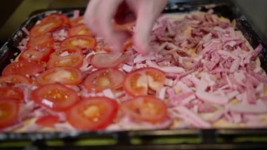 Ev yapımı pizza pişiren bir adam pizzanın içine taze doğranmış domates koyar.