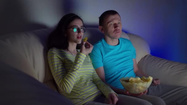 夜遅くまで若いですカップル見ますAムービーでテレビと食べるチップながら ソファに座って — ストック動画