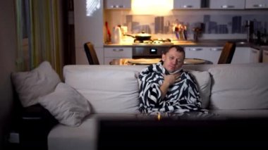 Soğuk algınlığı olan bir adam akşamları evde tek başına oturur ve televizyon izler.