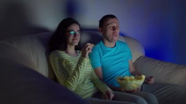 Kızla birlikte televizyonda komik bir film izleyen, cips yiyen ve gülen adam.