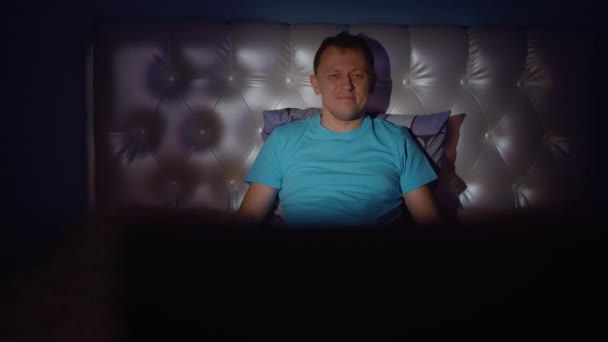 年轻人晚上坐在床上 看一部有趣的电影 放松的概念 镜头的移动 — 图库视频影像