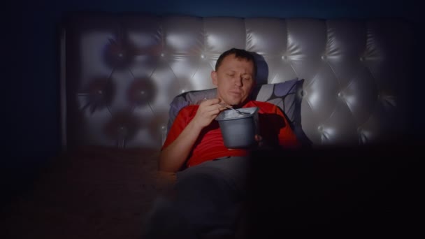 一个男人躺在床上吃着冰激凌 这是一个无聊的单身汉之夜 — 图库视频影像
