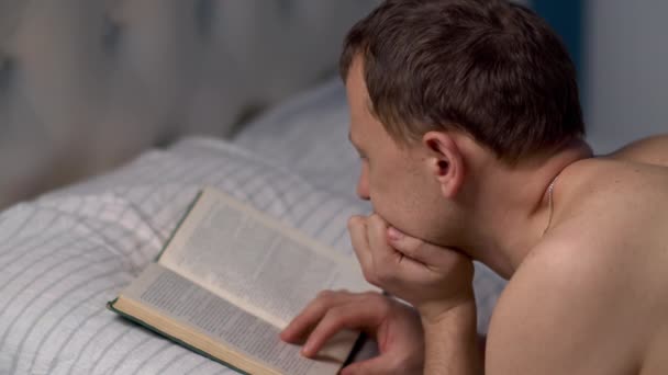 若い男はベッドに横になる前に本を読む — ストック動画