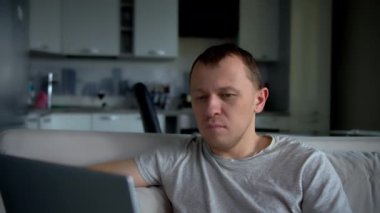 Bir adam evinde bir kanepede otururken dizüstü bilgisayarda çalışıyor.