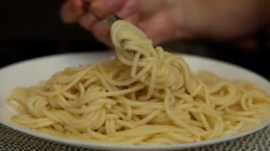 Taze pişmiş spagetti dolu beyaz bir tabak, buhar gelir, bir adam bir çatala spagetti koyar ve yer.