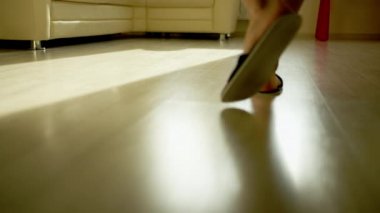 Terlikli bir adam parlak bir zeminde yürür ve bir kanepeye oturur.