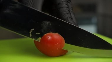 Büyük bir yemek bıçağıyla domates dilimlemek, siyah eldivenli bir adam, yakın plan.