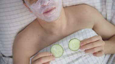 Yüzünde kozmetik bir maske ve gözlerinde salatalık dilimleri olan çekici bir adam.