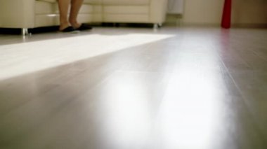 Terlikli bir adam kanepeden kalkar, parlak zeminde yürür, kamera hareket eder.