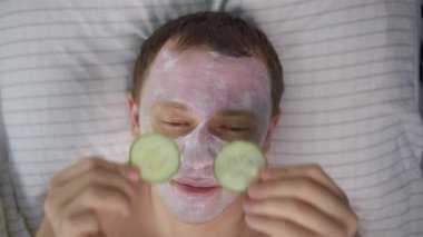 Yüzünde kozmetik maske ve gözlerinde salatalık dilimleri olan çekici bir adam.