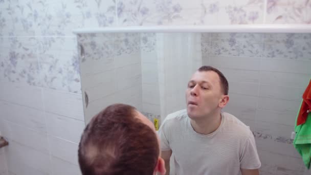 Un homme se tient dans la salle de bain devant un miroir et lui arrache les cheveux du nez — Video