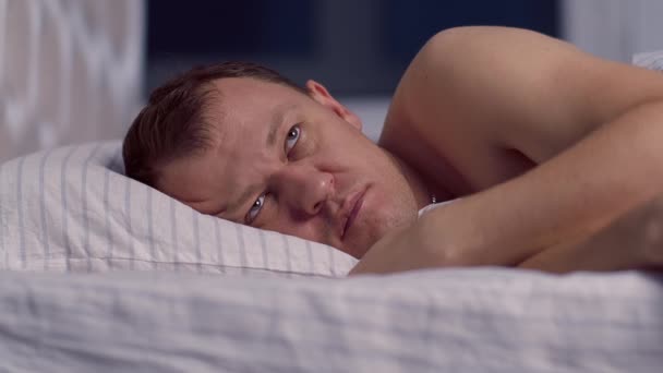 Мужчина лежит в постели поздно ночью и не может заснуть — стоковое видео