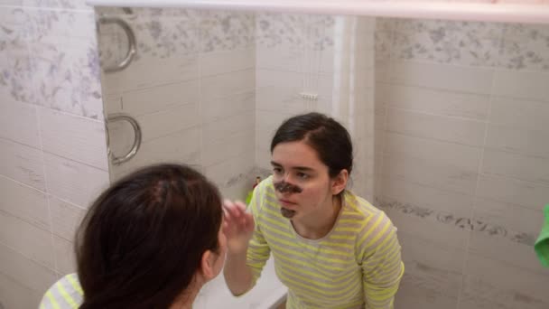 Yüzünde Siyah Kozmetik Maske Olan Genç Bir Kız Aynada Kendine — Stok video