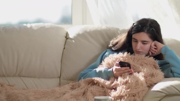 Симпатична Дівчина Брюнетка Сидить Дивані Вдень Читає Новини Своєму Телефоні — стокове відео