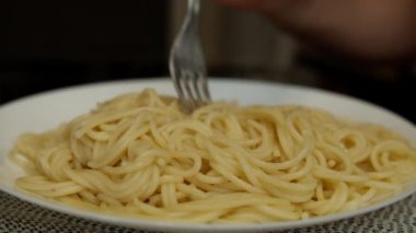 Çatalla yemek yiyen bir adam büyük beyaz bir tabaktan makarna yiyor.