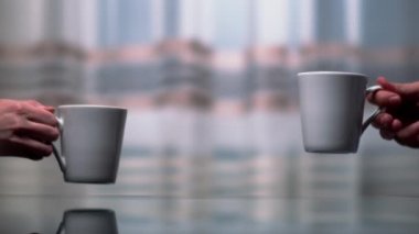 Erkeklerin ve kadınların elleri karanlık bir arka planda masa fincanlarının üzerine koyuyor.