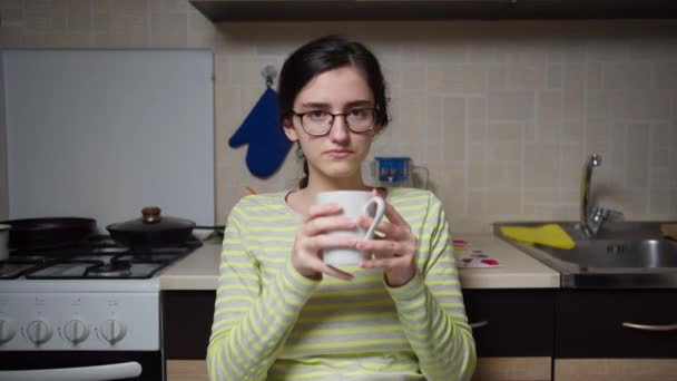 キッチンテーブルに座って白いセラミックマグカップから熱い飲み物を飲んでいます — ストック動画