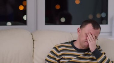 Genç adam geceleri kanepede oturur ve haberleri, olumsuz duyguları, kopyalama alanını, bir pencerenin arka planını izler.