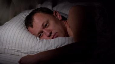 Genç bir adam uykusuz yatar, uyuyamaz, yastığı kırbaçlar, uyku bozukluğu kavramı.