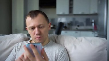 Elinde cep telefonuyla kanepede oturan adam internette iletişim kuruyor.