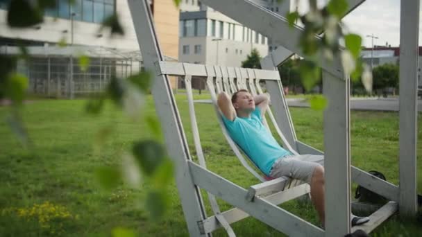 Een Jonge Man Rust Een Bank Een Zonnige Dag Camerabeweging — Stockvideo